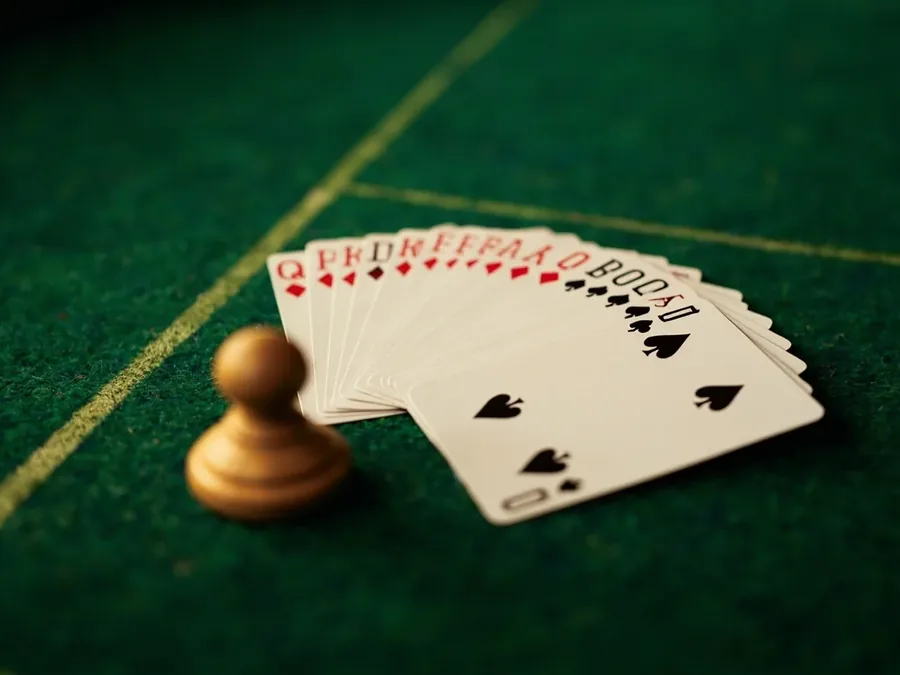 Editorial still-life of two neat stacks of rummy cards resting on green baize felt under warm directional light, felt weave and printed boundary visible